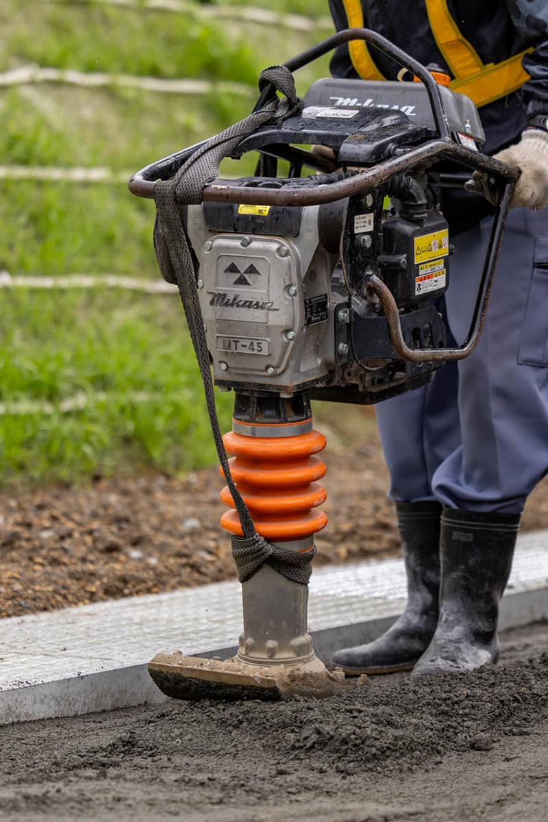 道路工事現場で白いヘルメットとオレンジ色の安全ベストを着た現場監督が、完成したばかりのアスファルト道路を確認している様子